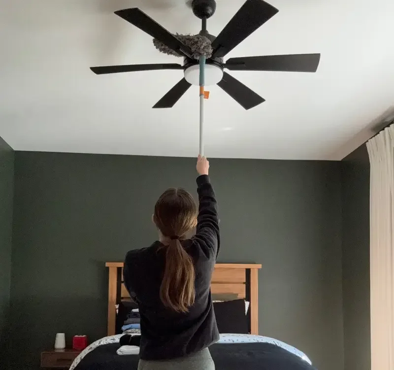 Cleaner dusting a ceiling fan with an extension duster during a deep clean